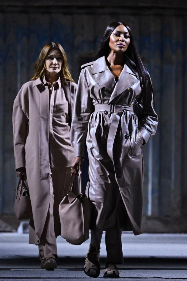 Naomi Campbell und ein weiteres Model präsentieren beigefarbene Trenchcoats und passende Handtaschen.