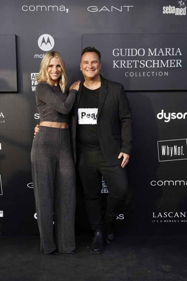 Guido Maria Kretschmer posiert mit einer Frau vor einer Wand mit Logos.