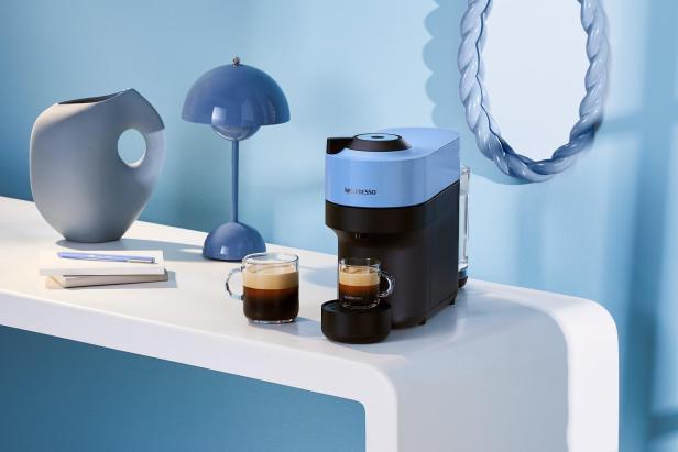 Eine blaue Nespresso-Maschine steht mit zwei Tassen Kaffee auf einem weißen Tisch.