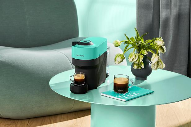 Eine türkisfarbene Nespresso-Maschine mit zwei Tassen Kaffee auf einem Tisch.