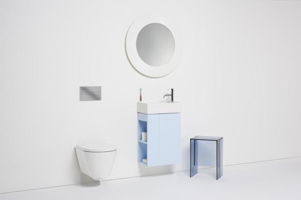 Ein Badezimmer mit Toilette, Waschbecken mit Unterschrank, Spiegel und einem Hocker.