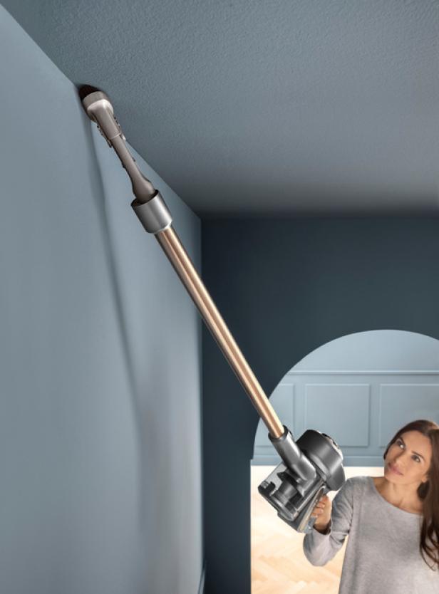 Eine Frau saugt mit einem Akku-Staubsauger die Decke ab.