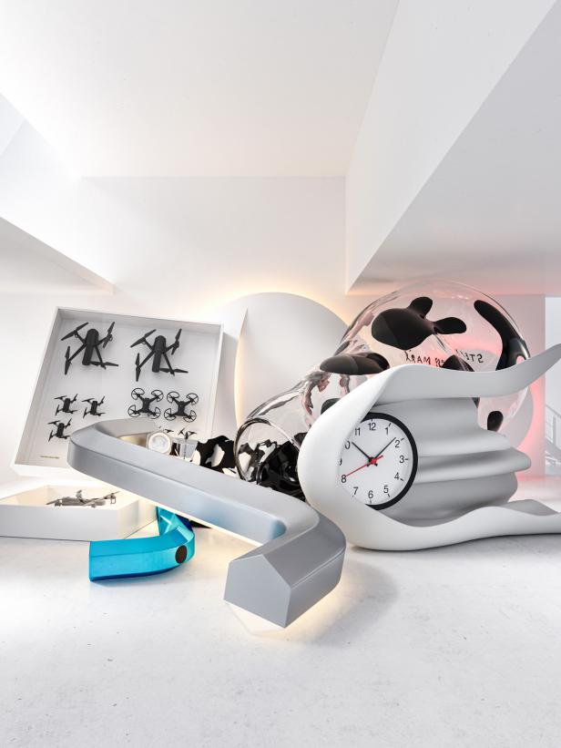 Eine futuristische Anordnung mit Drohnen, einer Uhr und abstrakten Formen in einem hellen Raum.