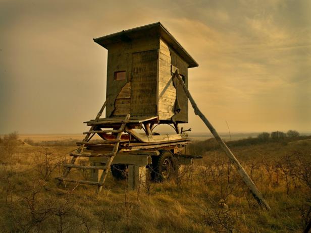 Ein hölzerner Hochsitz steht auf einem Anhänger in einer trockenen Landschaft.