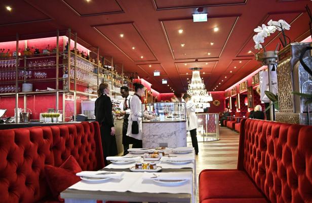 Das Interieur eines eleganten, rot dekorierten Restaurants mit Personal und Gästen.