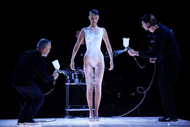 Bella Hadid wird auf einem Laufsteg von zwei Männern mit Farbe besprüht.