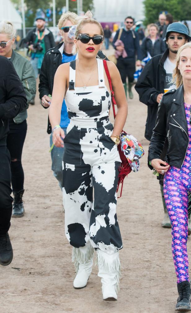 Rita Ora in einem schwarz-weiß gefleckten Overall und weißen Fransenstiefeln auf einem Festival.