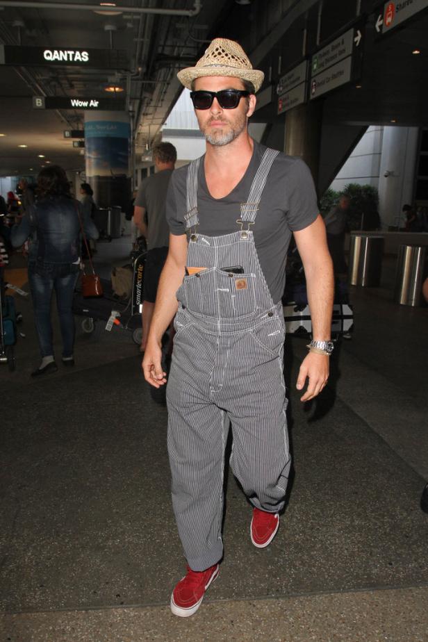 Ein Mann mit Hut und Latzhose geht durch einen Flughafen.