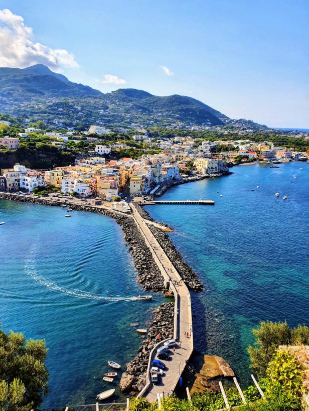 Blick auf Ischia mit einer langen Mole, die ins türkisfarbene Meer führt.