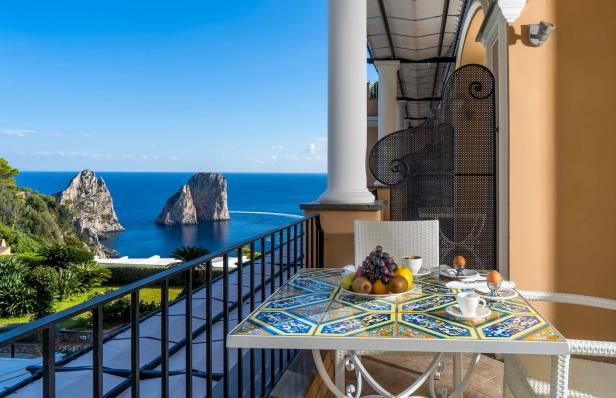 Blick von einem Balkon auf die Faraglioni-Felsen in Capri mit einem gedeckten Tisch.