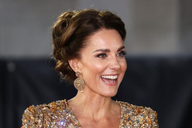 Kate Middleton lächelt und trägt ein goldenes, verziertes Kleid und Ohrringe.