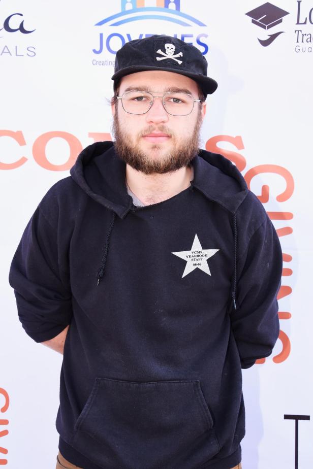 Ein Mann mit Brille und Bart trägt eine schwarze Kapuzenjacke und eine Mütze mit Totenkopf-Motiv.