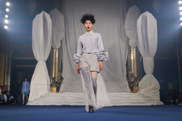 Ein Model präsentiert ein Outfit mit Rüschenärmeln auf einem Laufsteg.
