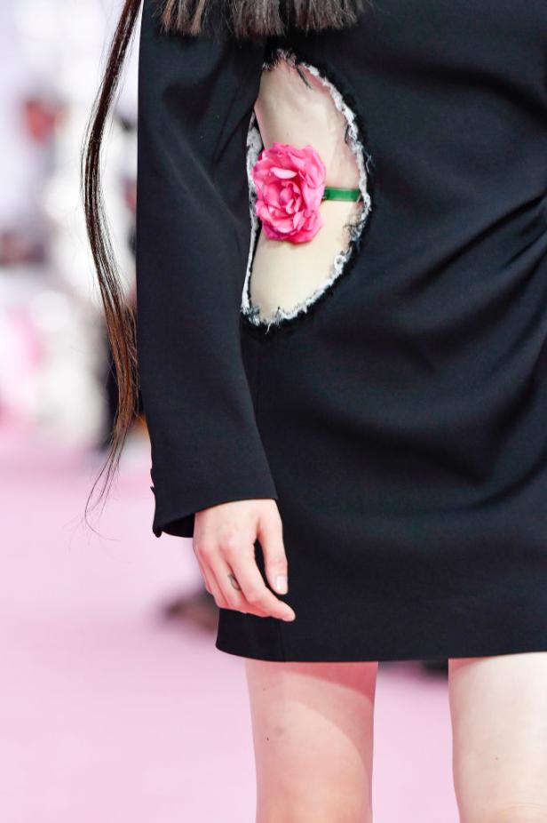Detailaufnahme eines schwarzen Kleides mit einem Loch, das mit einer rosa Rose verziert ist.