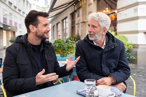 Zwei Männer sitzen an einem Tisch im Freien und unterhalten sich.