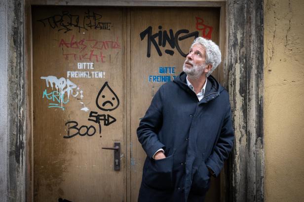 Ein Mann mit grauen Haaren steht vor einer mit Graffiti bedeckten Tür und schaut nach oben.