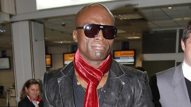 Der Sänger Seal mit Sonnenbrille und rotem Schal in einem Flughafen.