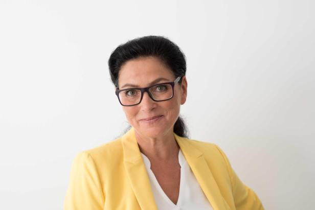 Eine Frau mit Brille und gelbem Blazer lächelt in die Kamera.