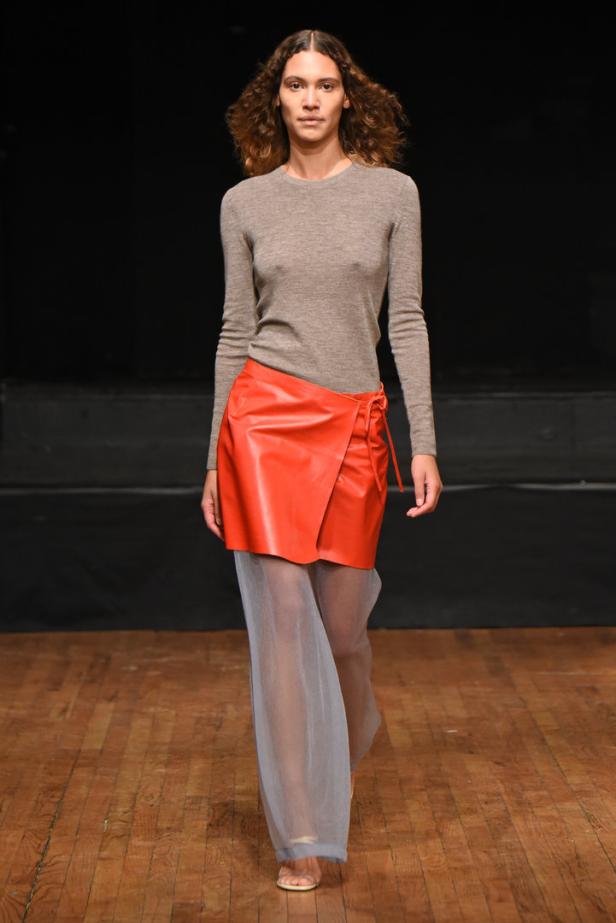 Eine Frau präsentiert eine orangefarbene Wickel-Minirock über einer transparenten Hose.