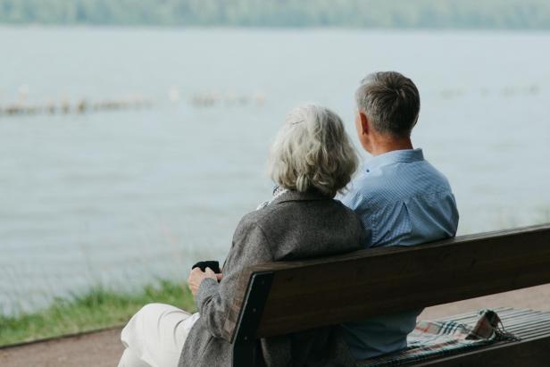 Älteres Paar sitzt auf einer Bank am See