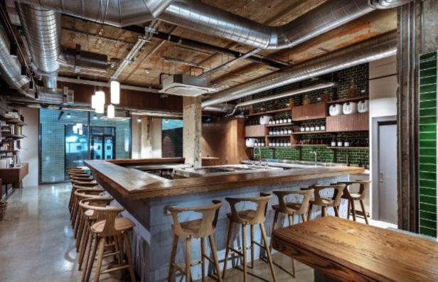 Eine Bar mit Holzhockern und Regalen mit Flaschen vor einer grünen Wand.
