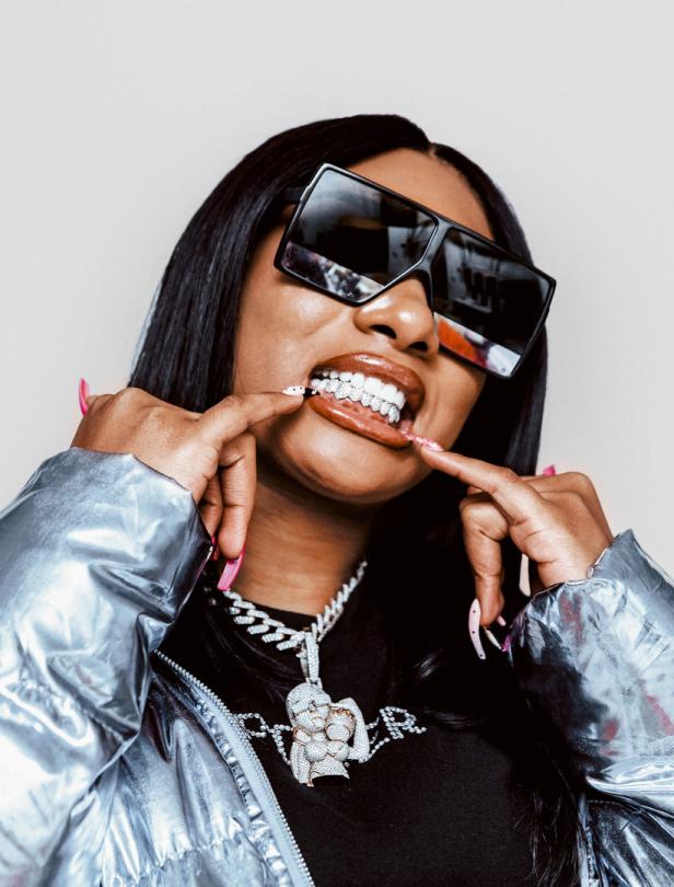 Megan Thee Stallion mit Grillz und übergroßer Sonnenbrille posiert für ein Foto.