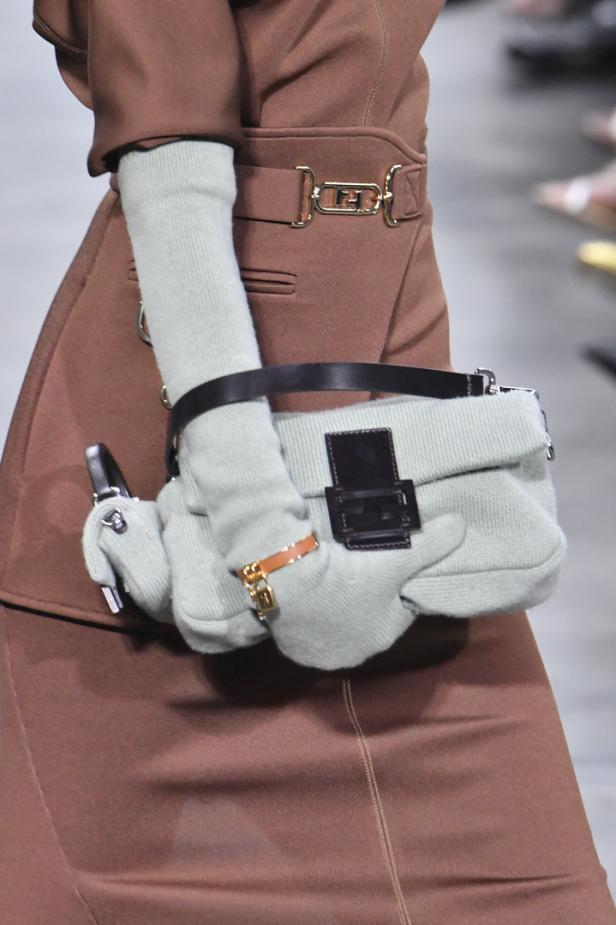 Eine Person in braunem Mantel hält eine hellgrüne Handtasche mit Handschuhen bedeckt.