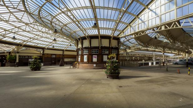 Die Wartehalle eines Bahnhofs mit einem Glasdach und dekorativen Blumentöpfen.