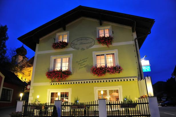 Das Gasthaus „Zum Blumentritt“ in Österreich mit blumengeschmückten Fenstern bei Nacht.