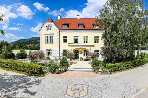 Das gelbe Gebäude des Weinguts Jamek in der Wachau mit rotem Dach und gepflegtem Garten.