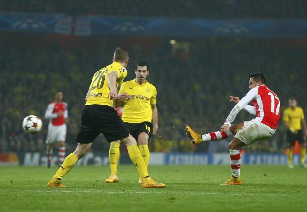 Ein Fußballspieler von Arsenal schießt den Ball, während Spieler von Borussia Dortmund zusehen.