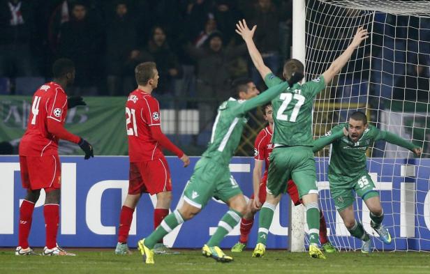 Fußballspieler in grünen Trikots jubeln vor dem Tor, während Spieler in roten Trikots zusehen.