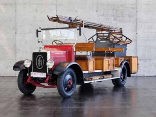 Ein Oldtimer-Feuerwehrauto mit Holzaufbau und Leiter auf dem Dach.