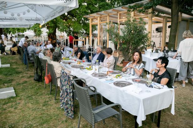 Eine Gruppe von Menschen sitzt an einer langen Tafel im Freien.