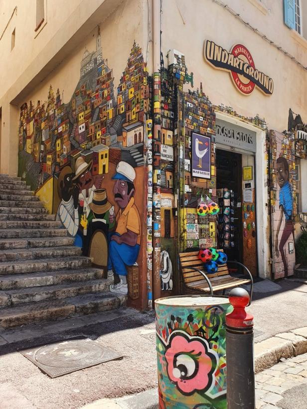 Eine belebte Straßenecke in Marseille mit Graffiti, Kunst und einem Geschäft namens „Undartground“.