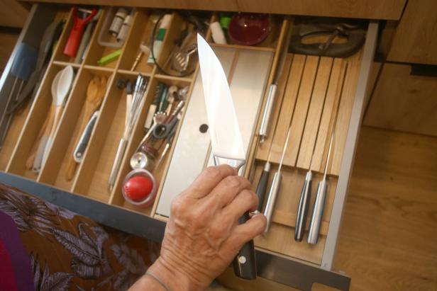 Eine Hand hält ein Messer vor einer Schublade mit Küchenutensilien.