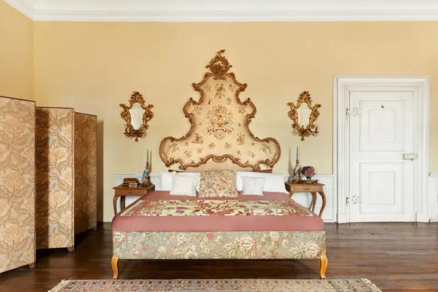 Ein Schlafzimmer mit einem verzierten Bett, einem Raumteiler und goldenen Spiegeln.