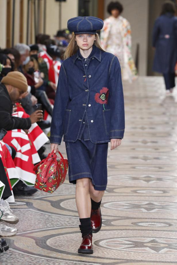 Eine Frau in einem Jeansensemble mit Mütze und roter Handtasche auf einem Laufsteg.