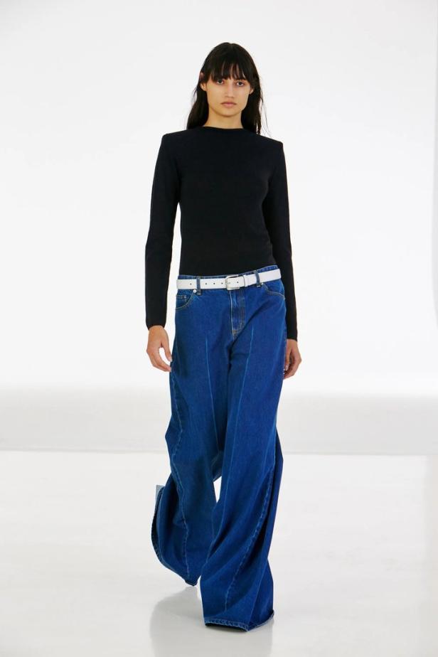 Eine Frau mit schwarzem Oberteil und sehr weiter, blauer Jeans mit weißem Gürtel.