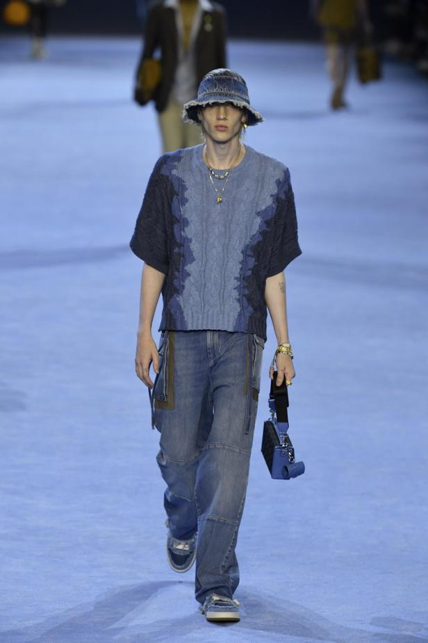Ein Model in Denim-Hut, Strickoberteil und Jeans auf einem Laufsteg.