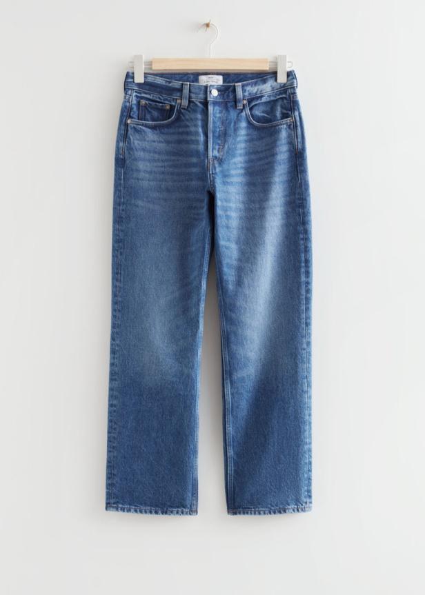 Eine blaue Jeans hängt an einem Holzbügel vor einem weißen Hintergrund.