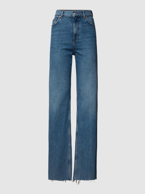 Eine blaue Jeans mit weitem Bein und ausgefranstem Saum vor einem grauen Hintergrund.