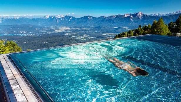 Eine Frau schwimmt in einem Infinity-Pool mit Blick auf eine Berglandschaft.