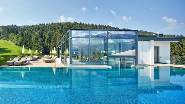 Ein Schwimmbad mit Liegestühlen vor einem modernen Gebäude mit Bergpanorama.