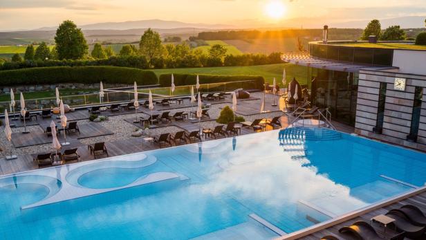 Ein Schwimmbad mit Liegestühlen und Sonnenschirmen bei Sonnenuntergang.