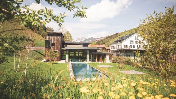 Ein modernes Haus mit Pool liegt in einer grünen Landschaft mit Bergen im Hintergrund.