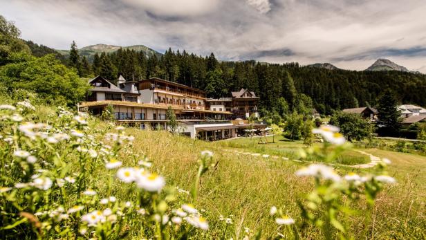 Ein Hotel liegt eingebettet in eine grüne Landschaft mit Wiesen und Bergen im Hintergrund.