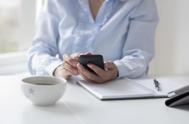 Eine Frau sitzt am Tisch und benutzt ihr Smartphone.