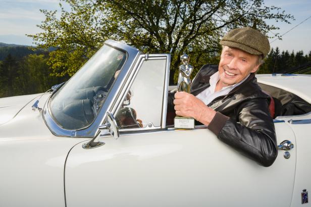 Peter Kraus sitzt in einem weißen Oldtimer-Cabriolet und hält eine Romy-Trophäe in der Hand.