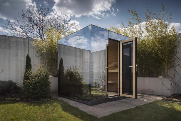 Eine moderne Sauna mit Glaswänden steht in einem Garten.